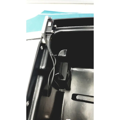 Black plastic car trunk lid latch mechanism with metallic components on the back of defibrillator storage cabinet wall mount