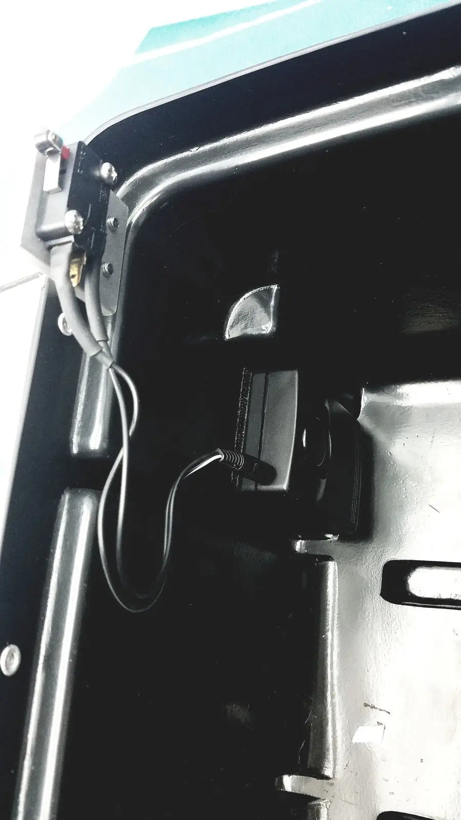 Black rectangular camera mounted inside vehicle interior with wiring and metal brackets on defibrillator storage cabinet wall mount