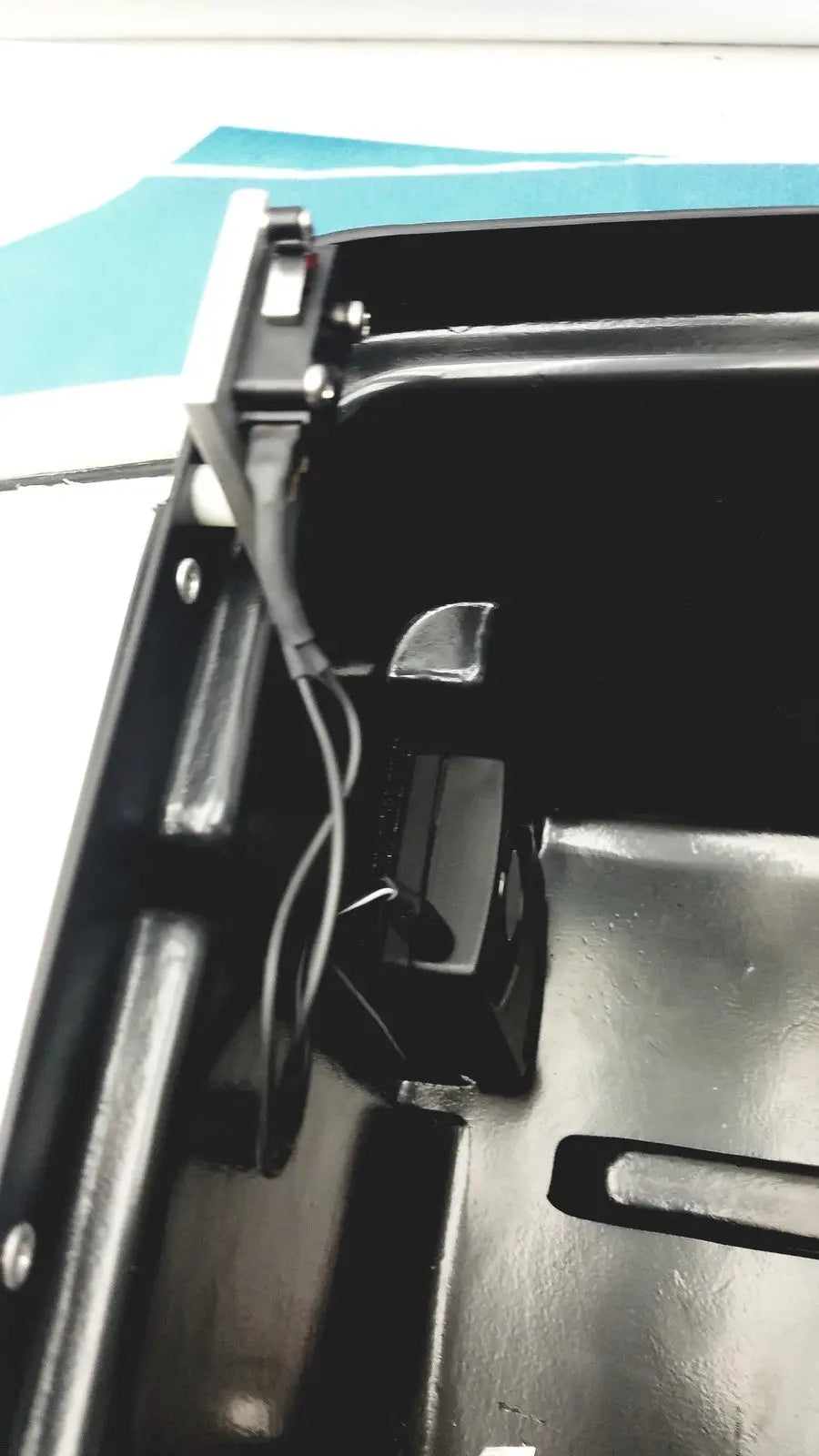 Black plastic car trunk lid latch mechanism with metallic components on the back of defibrillator storage cabinet wall mount