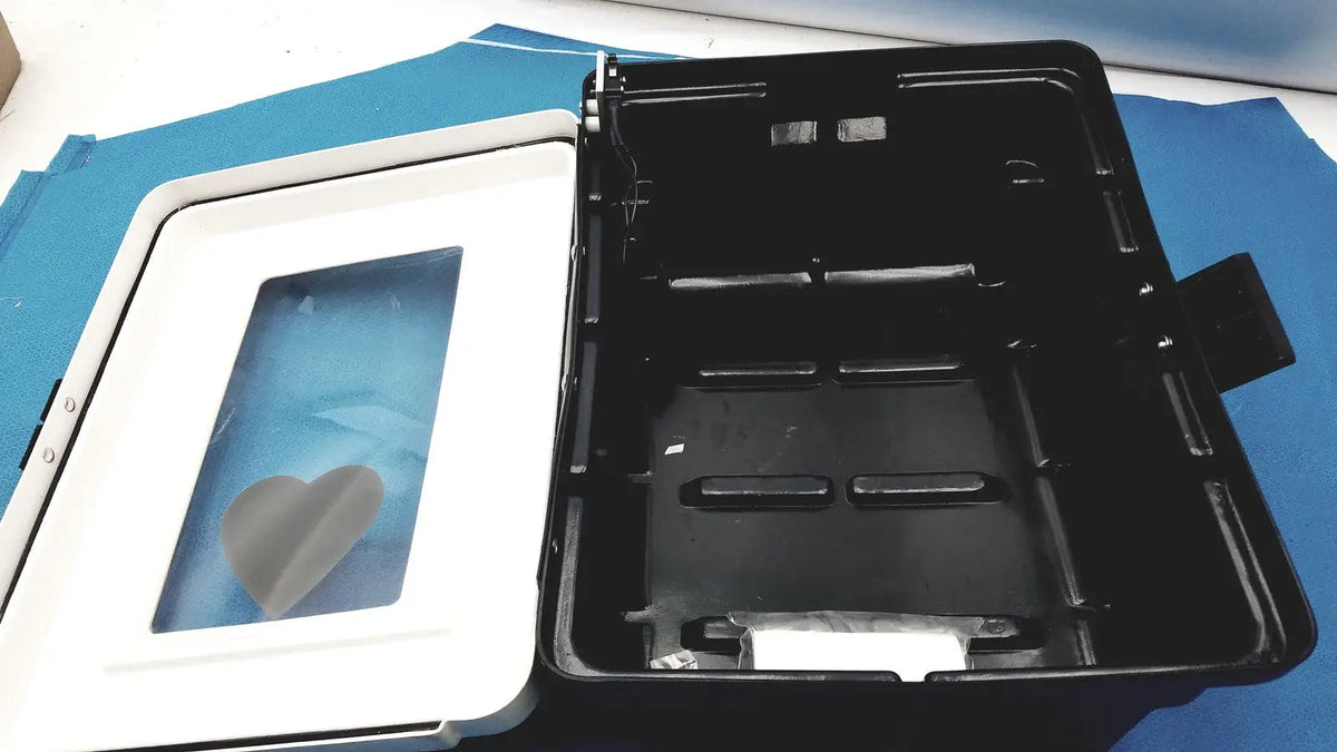 Black plastic defibrillator storage cabinet with white lid and heart-shaped window for cabinet wall mount use