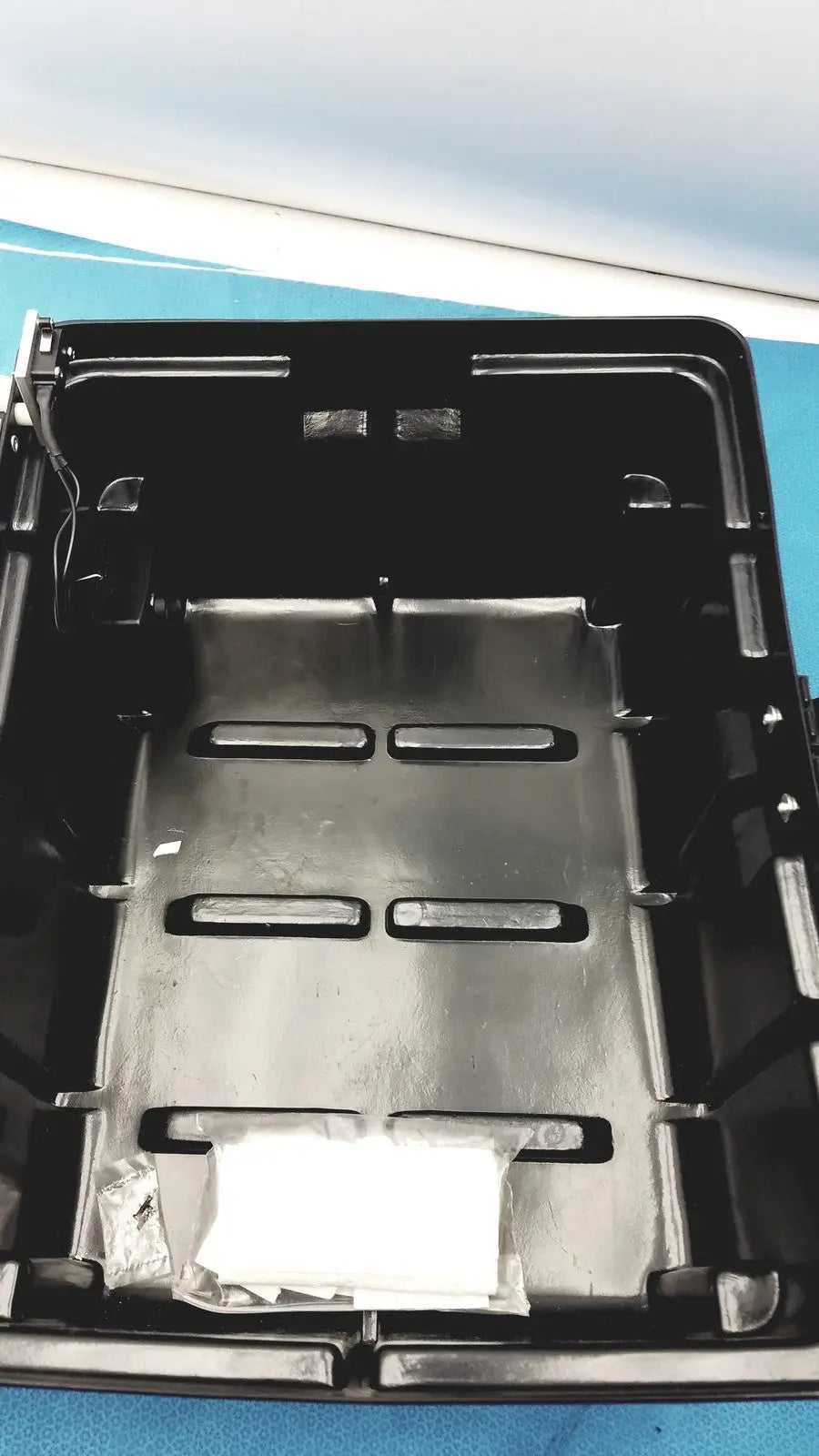 Black plastic underbody tray with molded compartments and metallic insert for defibrillator storage cabinet wall mount
