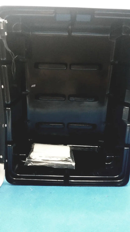 Black plastic defibrillator storage cabinet wall mount with molded compartments and a small wrapped item inside
