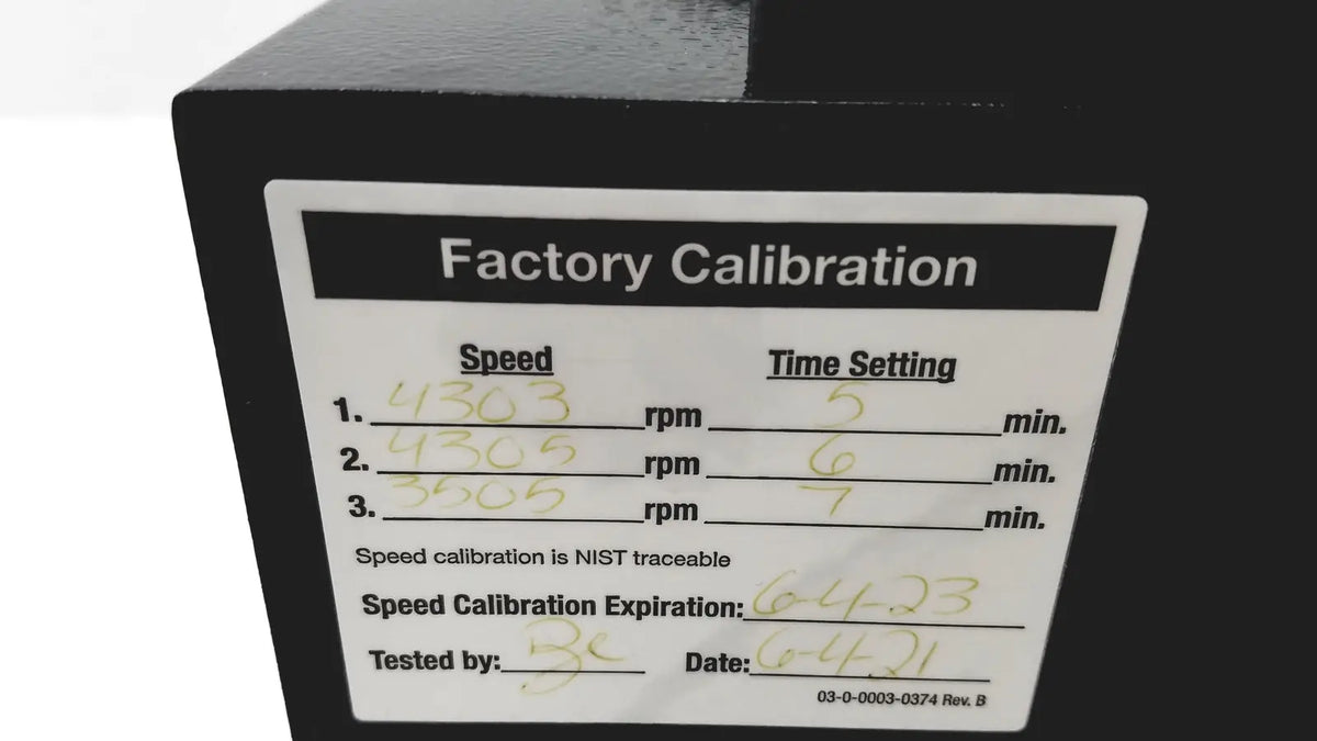 Black industrial machine with white factory calibration label showing handwritten data and nist traceable certification on drucker diagnostics dash apex 24 centrifuge