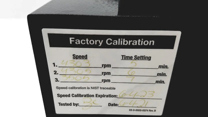 Black industrial machine with white factory calibration label showing handwritten data and nist traceable certification on drucker diagnostics dash apex 24 centrifuge