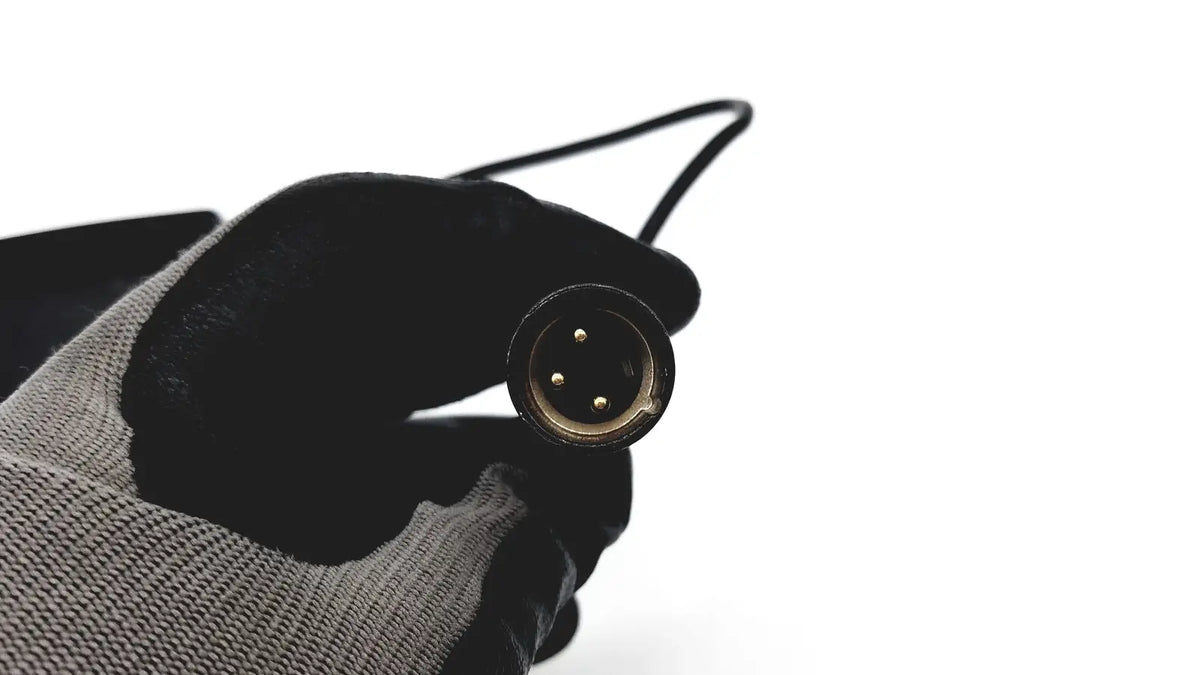 Black-gloved hand holding black xlr audio cable connector with three gold-plated pins for eds adaptor charger reuse medical