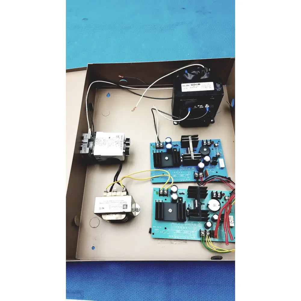 Black transformer with white label and blue terminal screws mounted inside cardboard electrical control panel enclosure