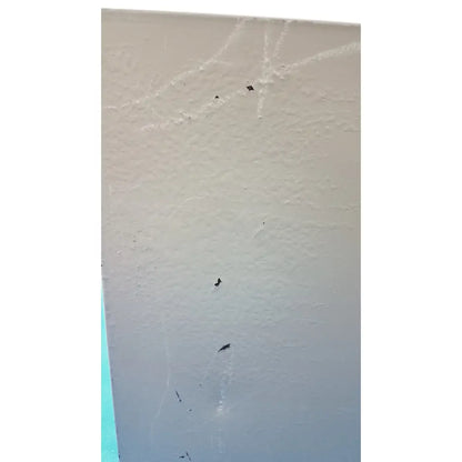 Beige textured wall with faint white scratches and black specks on the back of an electrical control panel with time delay relay