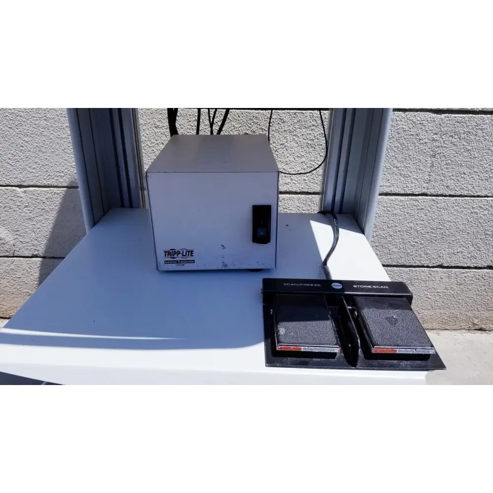 White metal tripp lite power strip with black foot pedal scanner on white surface for ellex eyecubed ultrasound biomicroscopy system