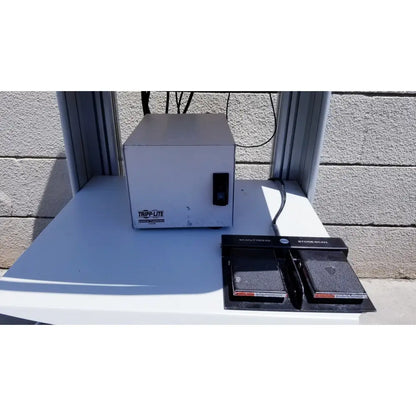 White metal tripp lite power strip with black foot pedal scanner on white surface for ellex eyecubed ultrasound biomicroscopy system