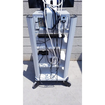 White metal cart with wheels and shelves holding electronic equipment and tangled cables for ellex eyecubed ultrasound biomicroscopy system