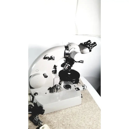 Silver and black compound microscope with dual eyepieces and adjustable stage alongside eppendorf centrifuge 5415 r reuse medical equipment