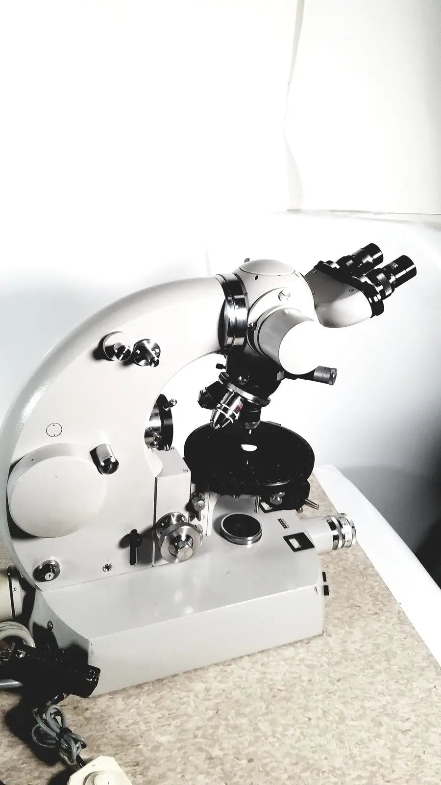 Silver and black compound microscope with dual eyepieces and adjustable stage alongside eppendorf centrifuge 5415 r reuse medical equipment