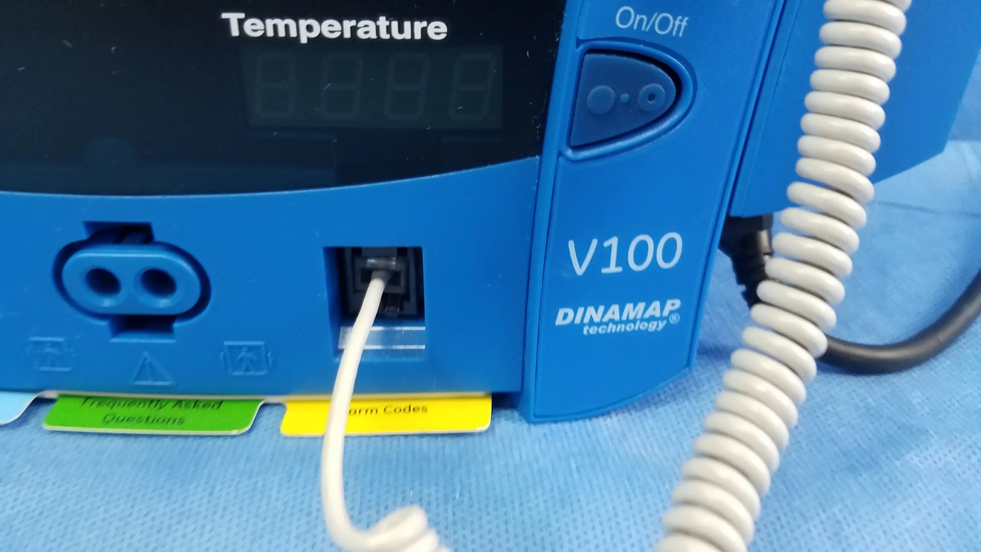 Blue GE Dinamap V100 vital signs patient monitor with nibp cuffs, coiled white cable, labeled adhesive strips, and power adapter