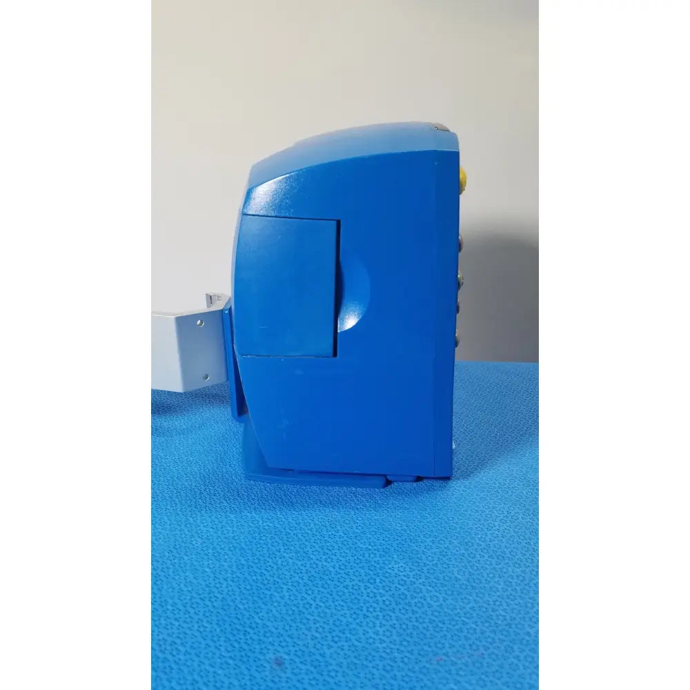 Blue plastic electric pencil sharpener with hinged lid and yellow button shown with GE Healthcare v180-jbac-axaa-xx vital signs monitor