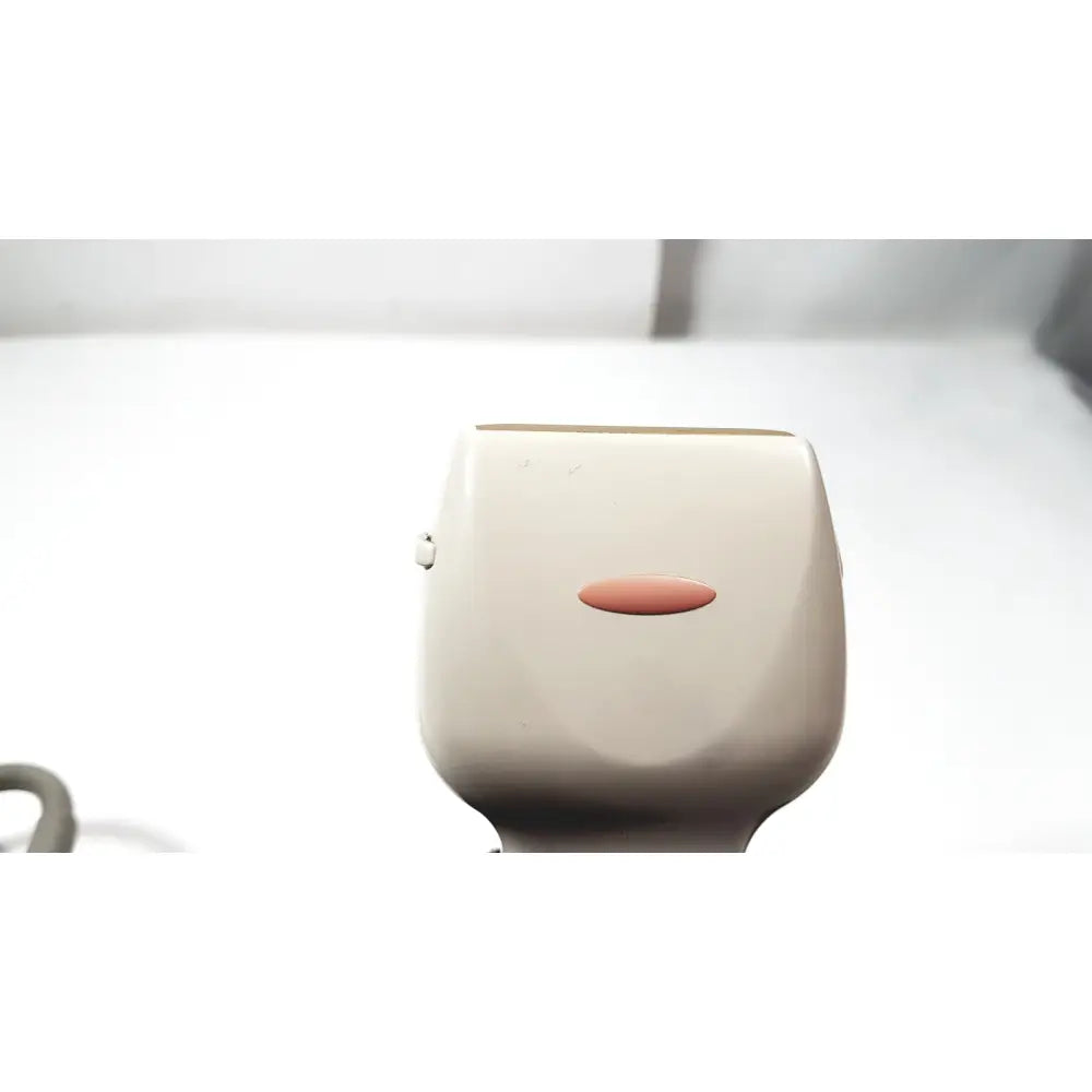 Beige electric epilator with smooth rounded body and oval power button shown alongside ge medical systems ultrasound convex array transducer