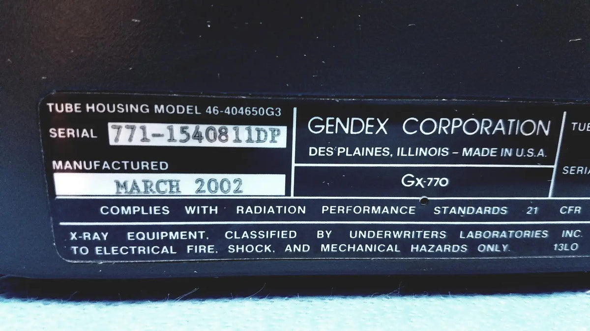Black plastic label with white text on gendex 770 tube head detailing model and manufacturer for imaging equipment reuse medical