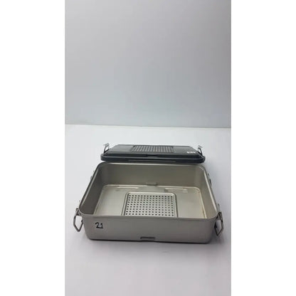 Genesis solid brass sterilization container with silver stainless steel tray, black perforated lid, and side handles