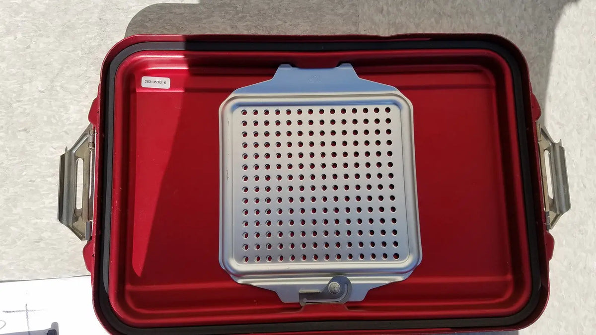 Silver perforated grill grate resting inside red genesis sterilization container half lid for secure sterilization storage