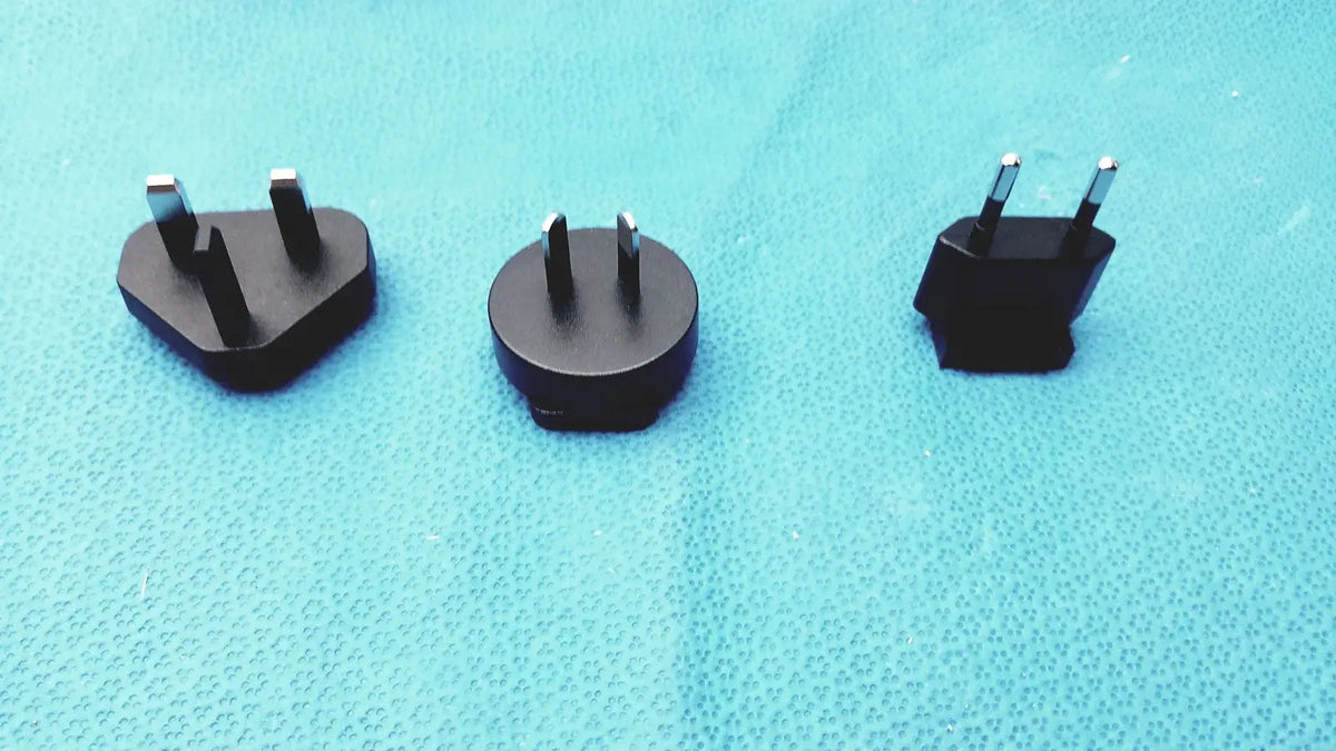 Three black travel plug adapters with metallic prongs for international use compatible with glidescope video monitor an162878