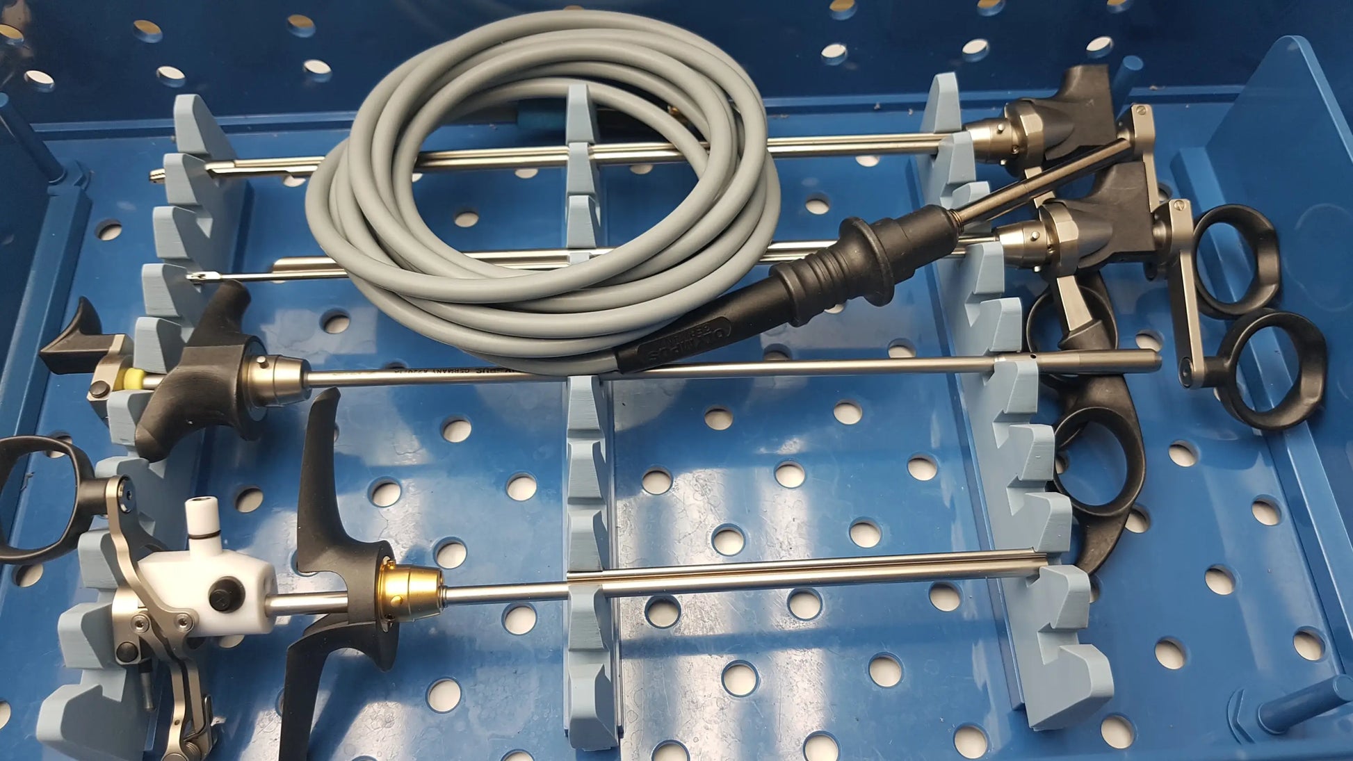 Gray coiled surgical instrument with black and metallic components in blue perforated tray from gyrus acmi instrument set