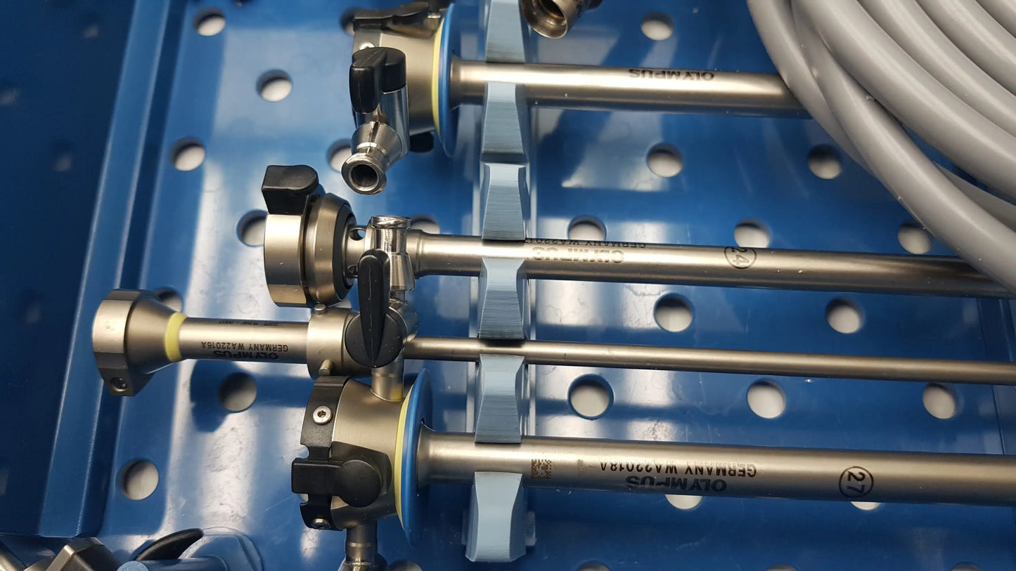 Silver surgical instruments with black knobs and engraved markings neatly arranged in blue gyrus acmi st-cr2 endoscope storage tray with olympus telescopes
