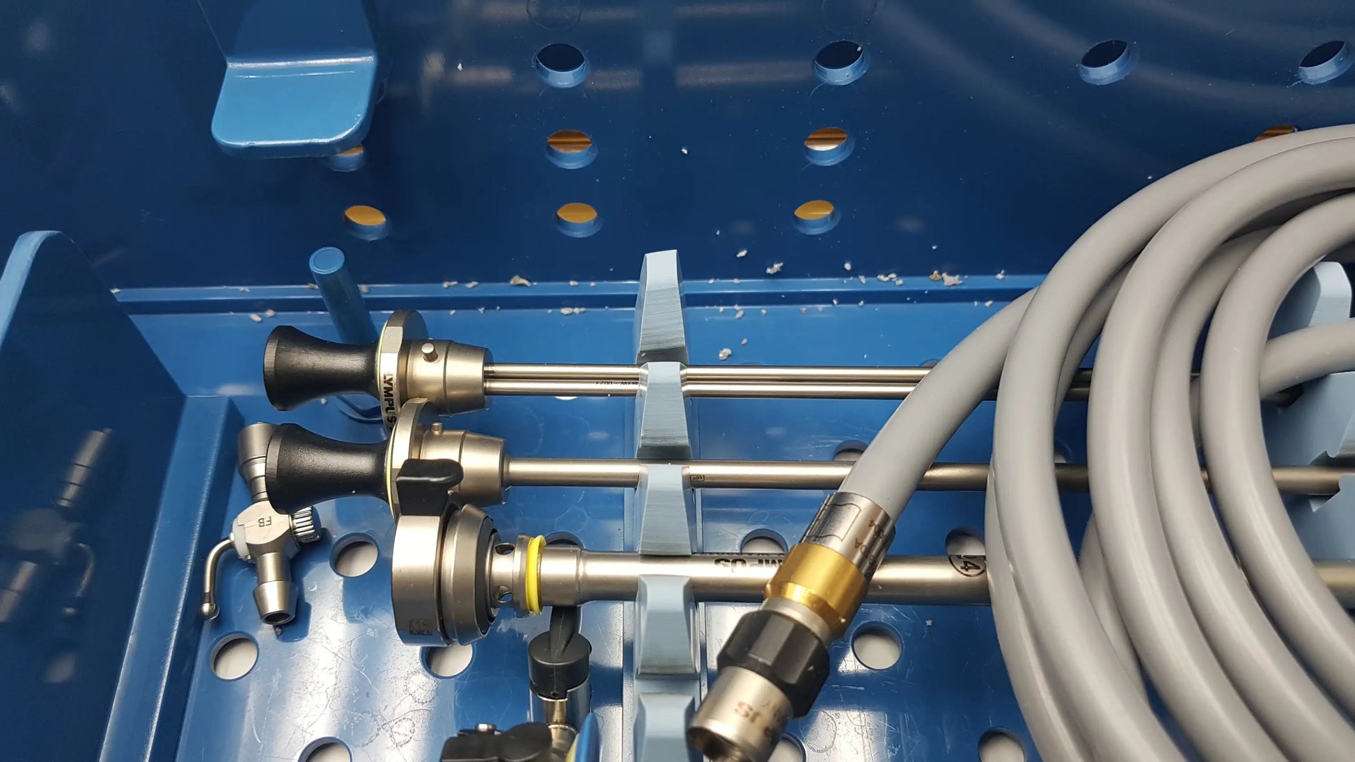 Gray medical endoscope cables with metallic connectors neatly arranged in blue gyrus acmi endoscope storage sterilization tray with olympus telescopes