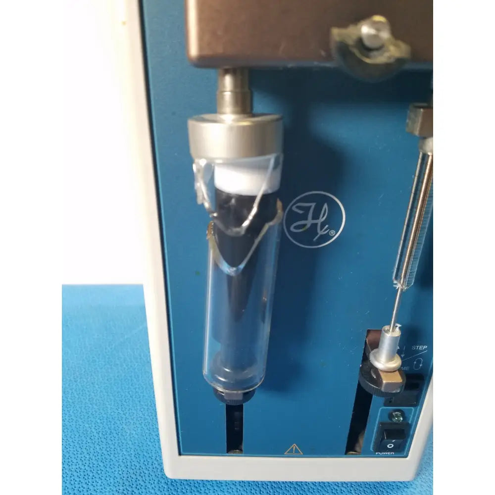 A clear glass vial with silver cap and black interior mounted on a blue hamilton microlab series syringe pump dispenser