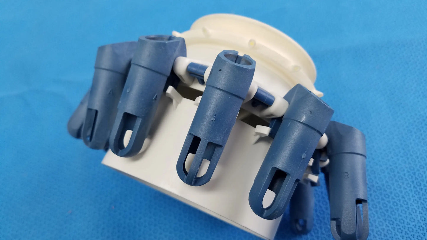 Blue plastic robotic hand with articulated fingers mounted on beige base next to helmer centrifuge rotor with tube inserts