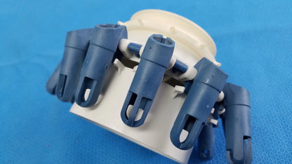 Blue plastic robotic hand with articulated fingers mounted on beige base next to helmer centrifuge rotor with tube inserts
