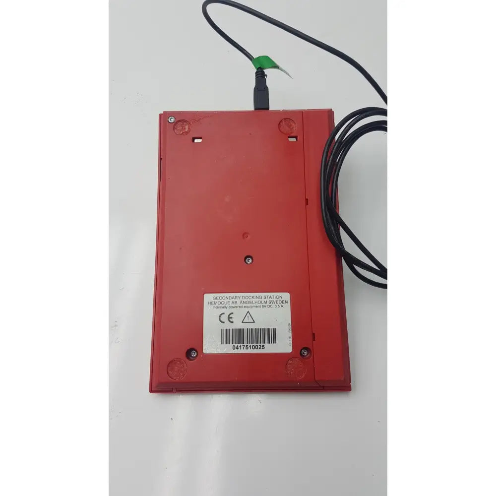 Red plastic secondary docking station with black cable attached to hemocue hb 201 dm hemoglobin system analyzer for reuse medical purposes
