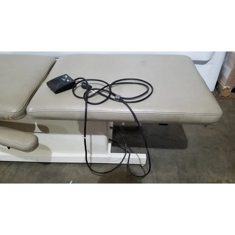 Beige padded physical therapy treatment table with black power cord and foot pedal hill model ha90pt