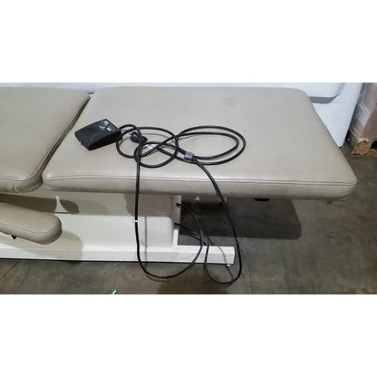 Beige padded physical therapy treatment table with black power cord and foot pedal hill model ha90pt