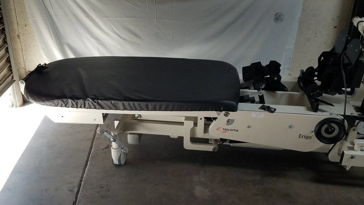 White hocoma erigo pro robotic tilt table with black padded surface and casters for verticalization therapy