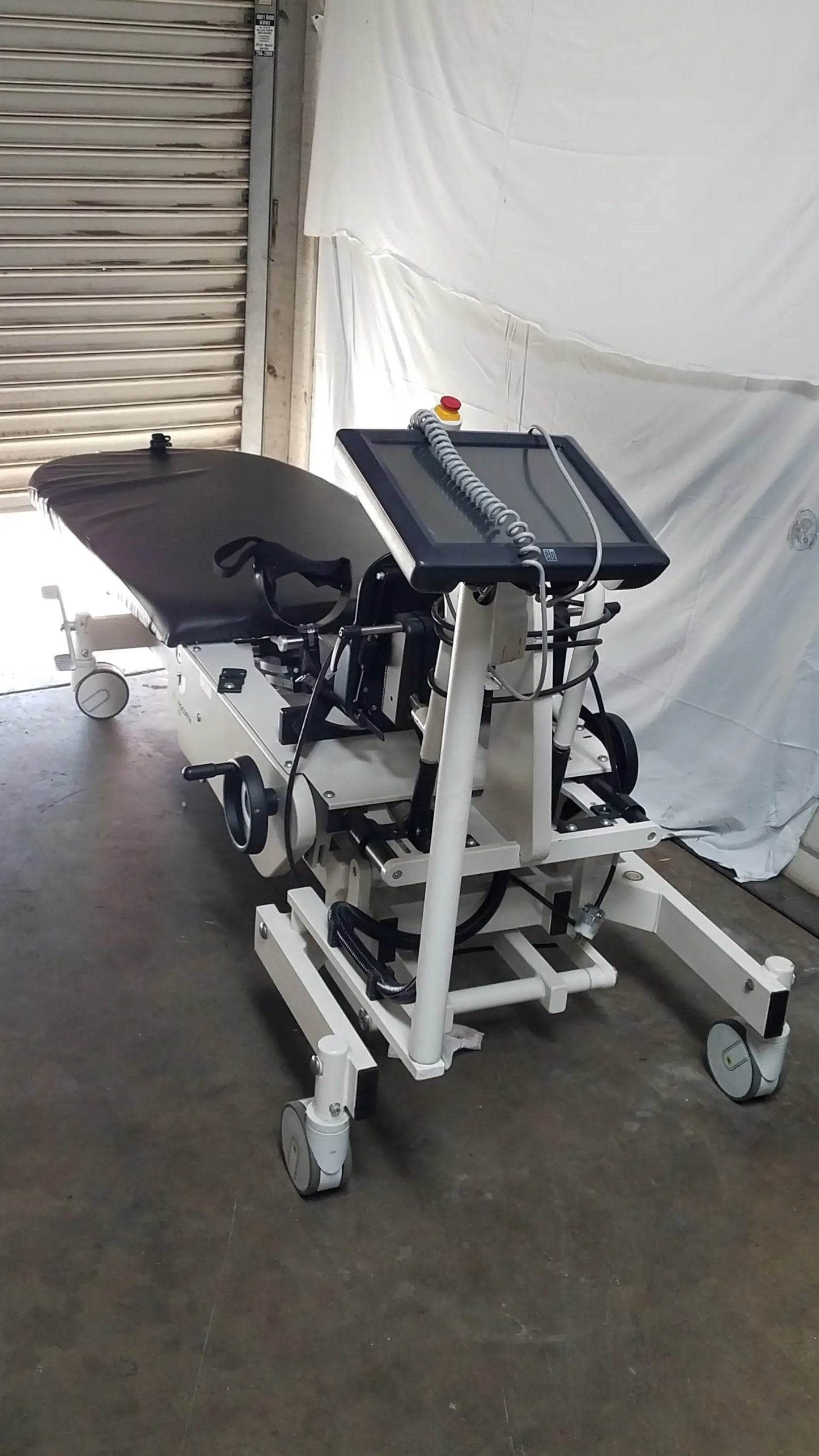 Hocoma erigo pro robotic tilt table with black padded surface, white metal frame, and mounted touchscreen monitor