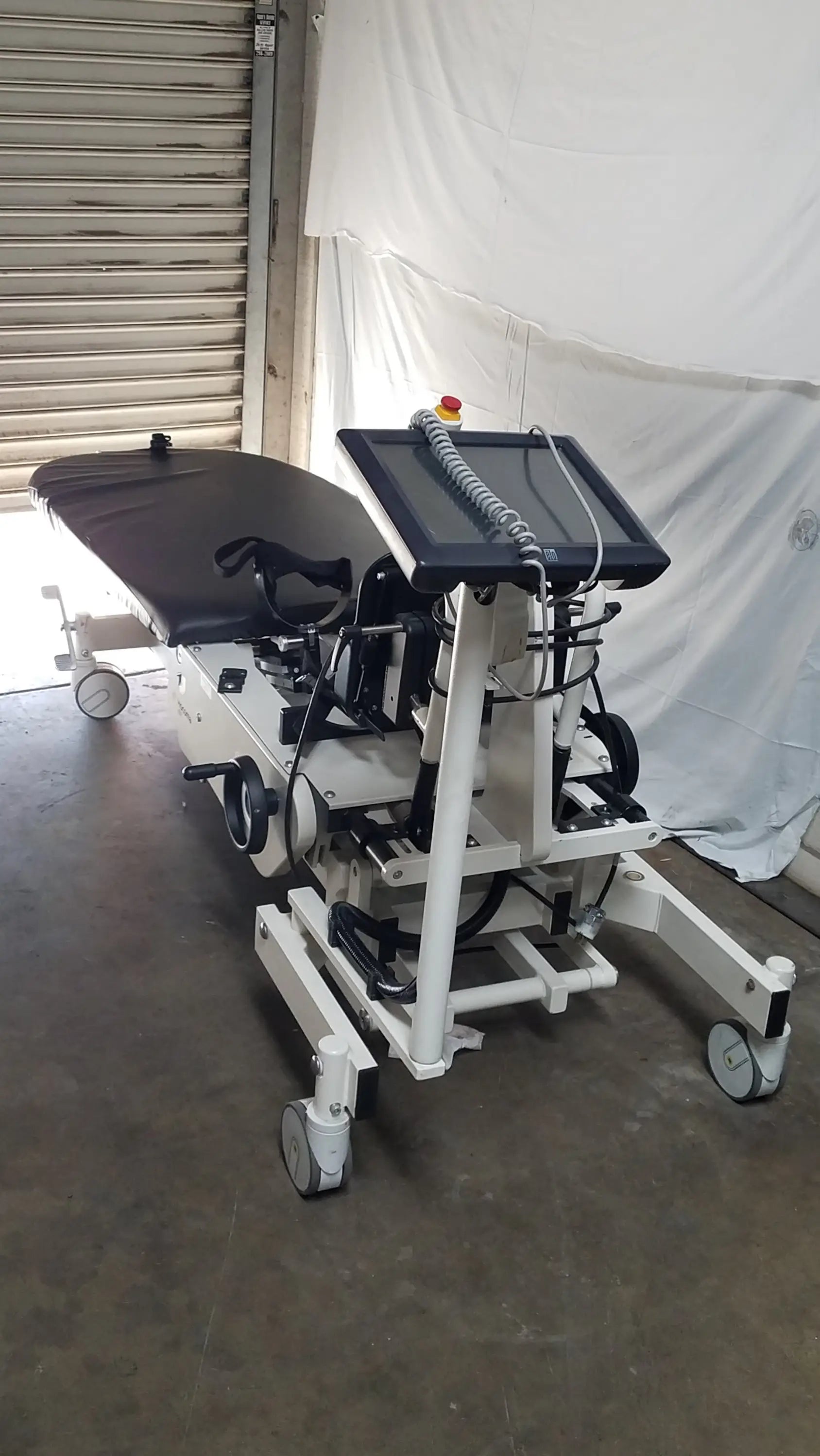Hocoma erigo pro robotic tilt table with black padded surface, white metal frame, and mounted touchscreen monitor