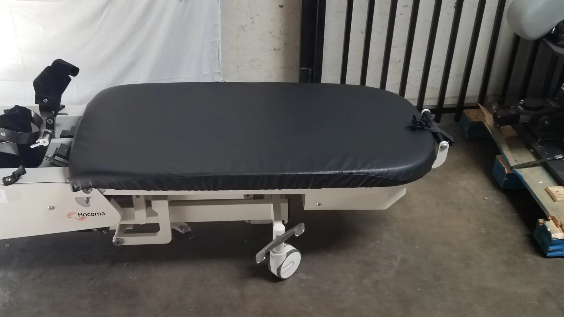 Black padded surface on white hologic robotic tilt table with adjustable features and caster wheels for verticalization therapy