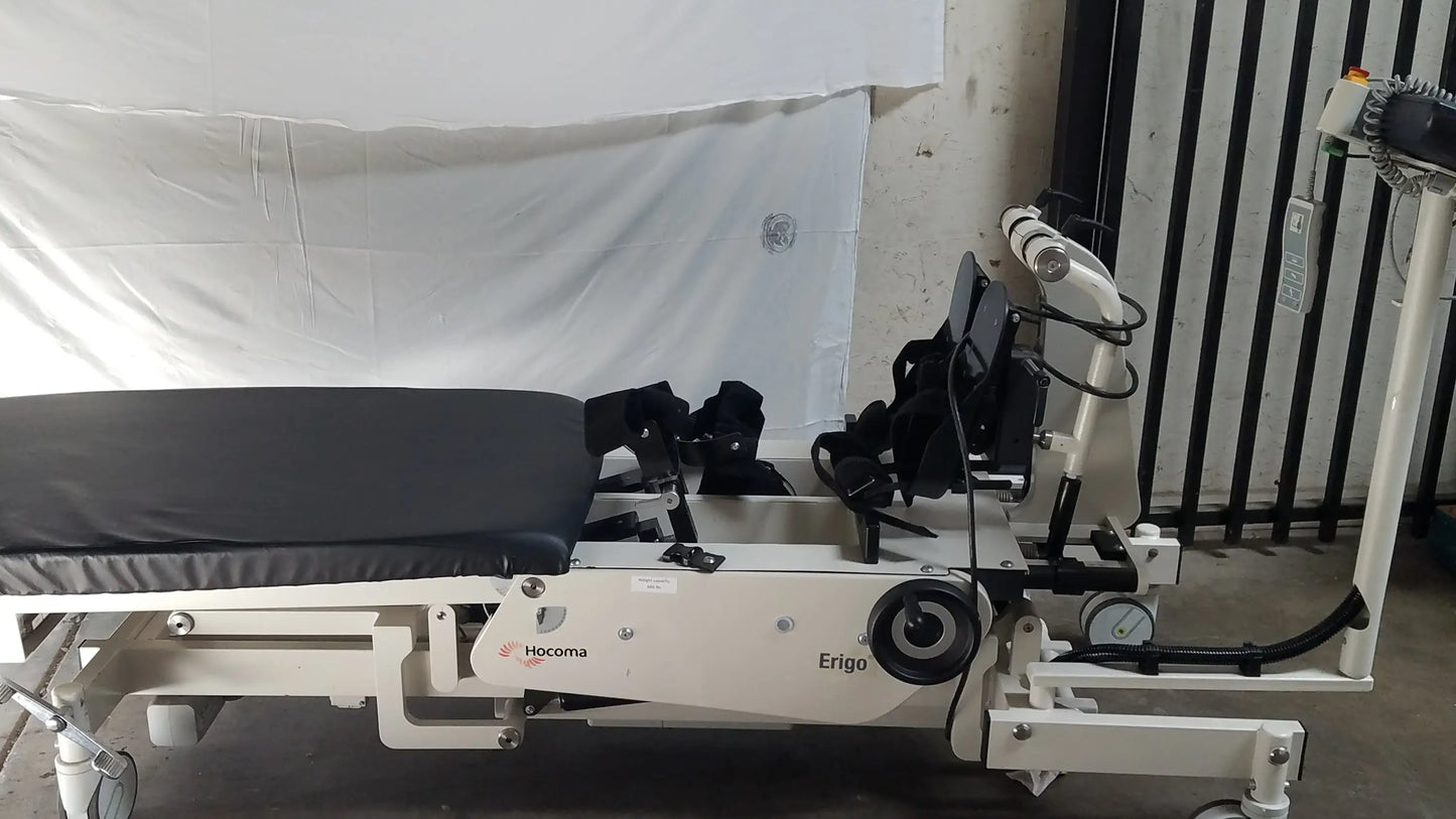 White hocoma erigo pro robotic tilt table with black padded surface and adjustable mechanical arms for verticalization therapy