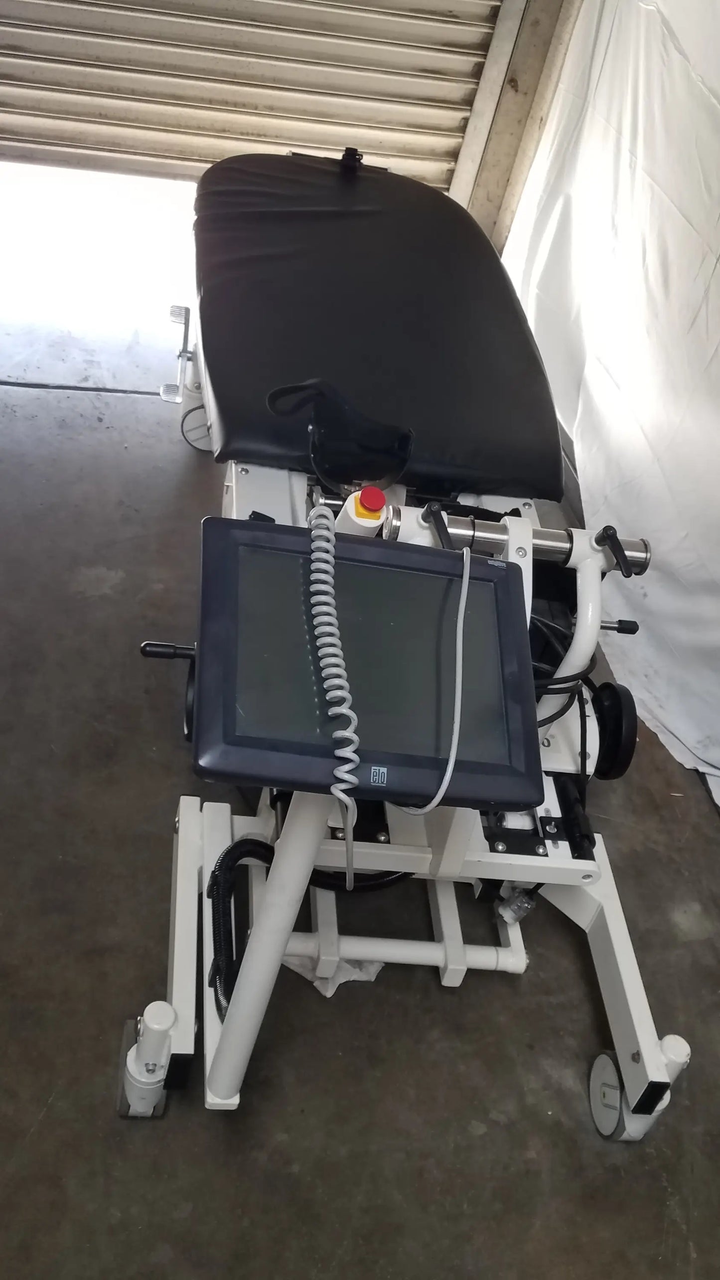 Medical examination table with black padded surface white metal frame and mounted touchscreen monitor in Hocoma Erigo Pro robotic tilt table