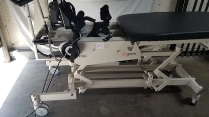 Beige hocoma ergo adjustable robotic tilt table with black padded surface and wheeled base for verticalization therapy