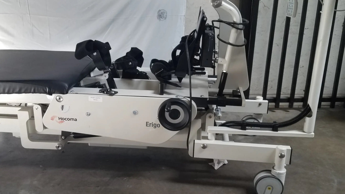 White hocoma erigo pro robotic tilt table with black padded sections and adjustable armrests for rehabilitation therapy