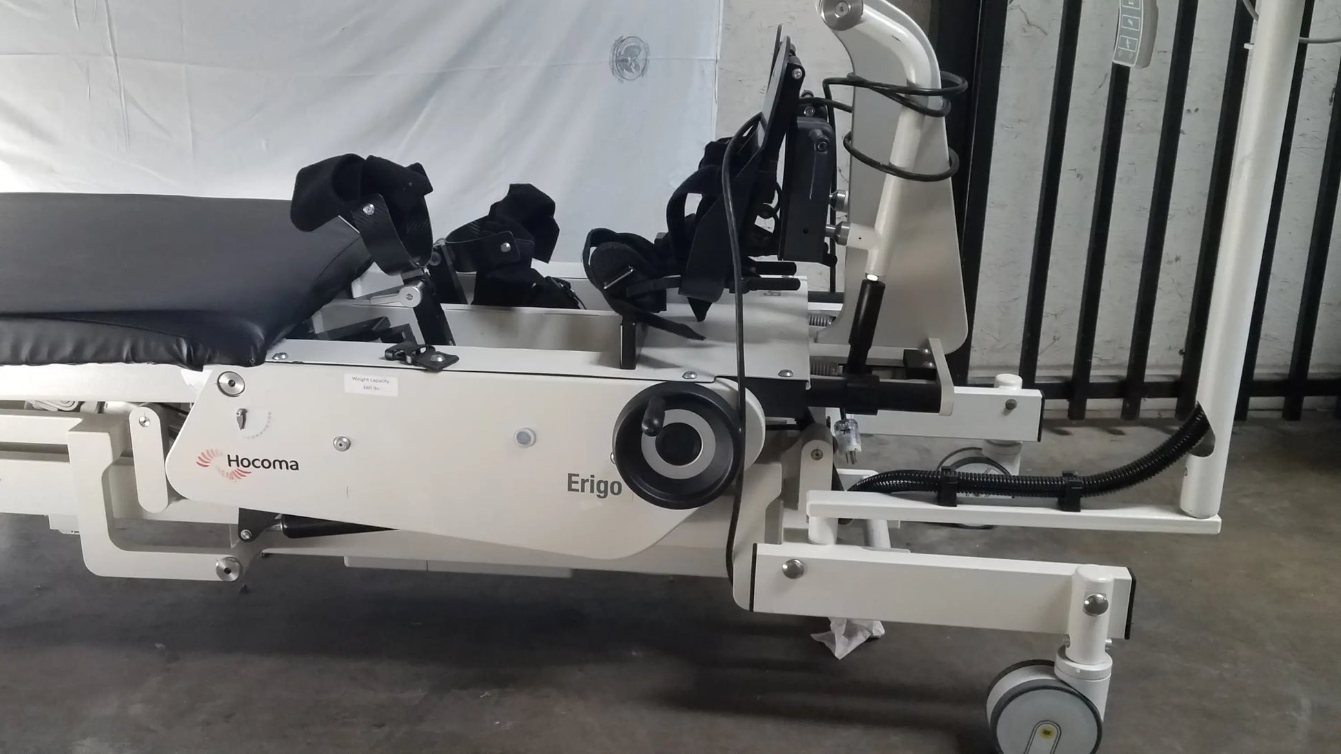 White hocoma erigo pro robotic tilt table with black padded sections and adjustable armrests for rehabilitation therapy