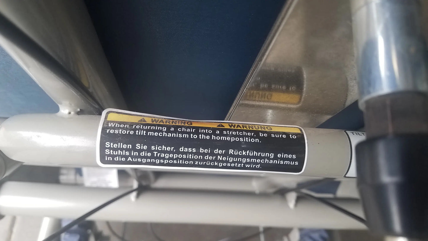 Black and yellow warning label with bilingual text on metallic cylindrical component of humanCare I-400 bariatric convertible chair