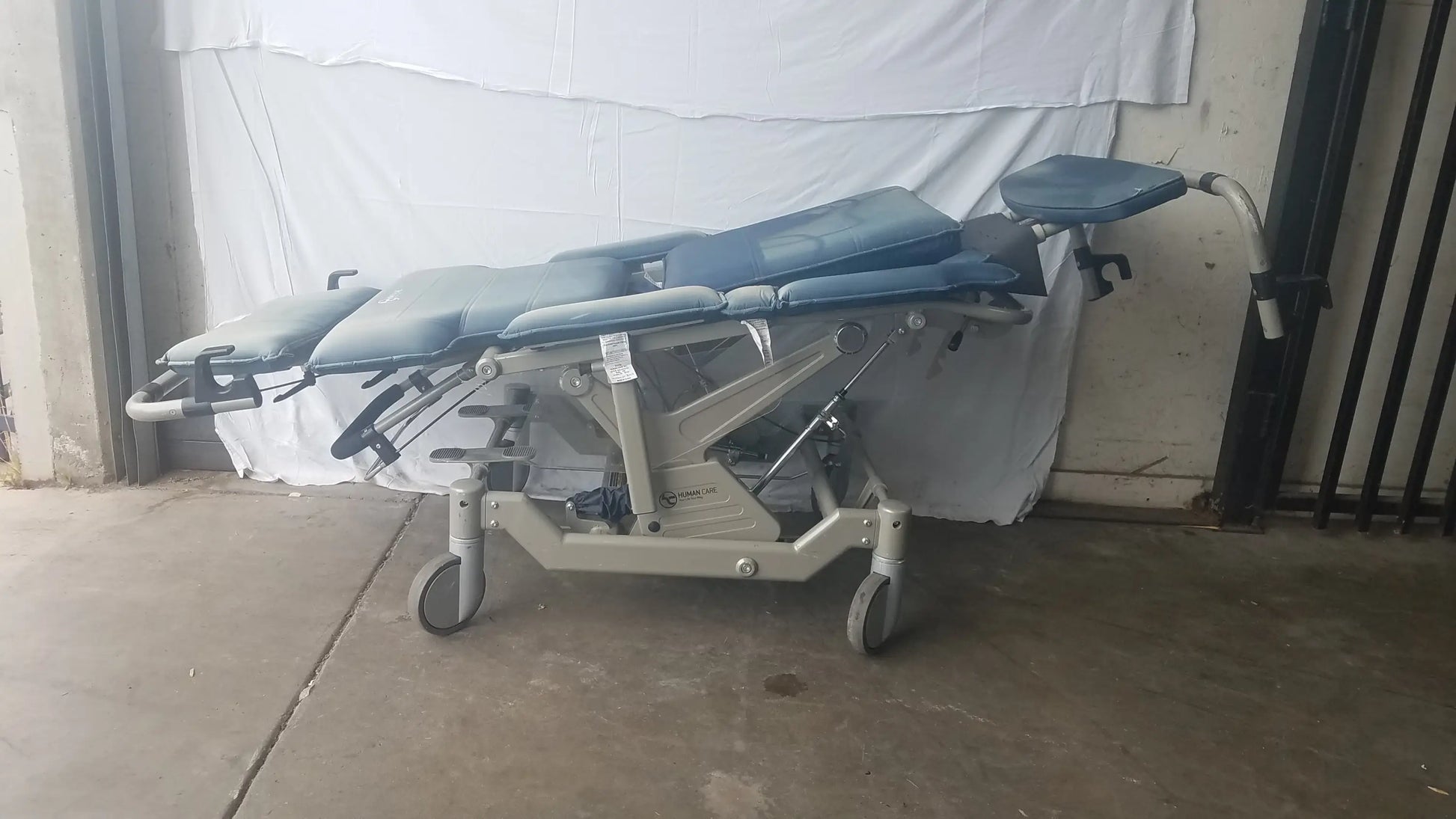 Blue padded humanCare I-400 bariatric convertible chair with metallic frame and wheels for medical examinations