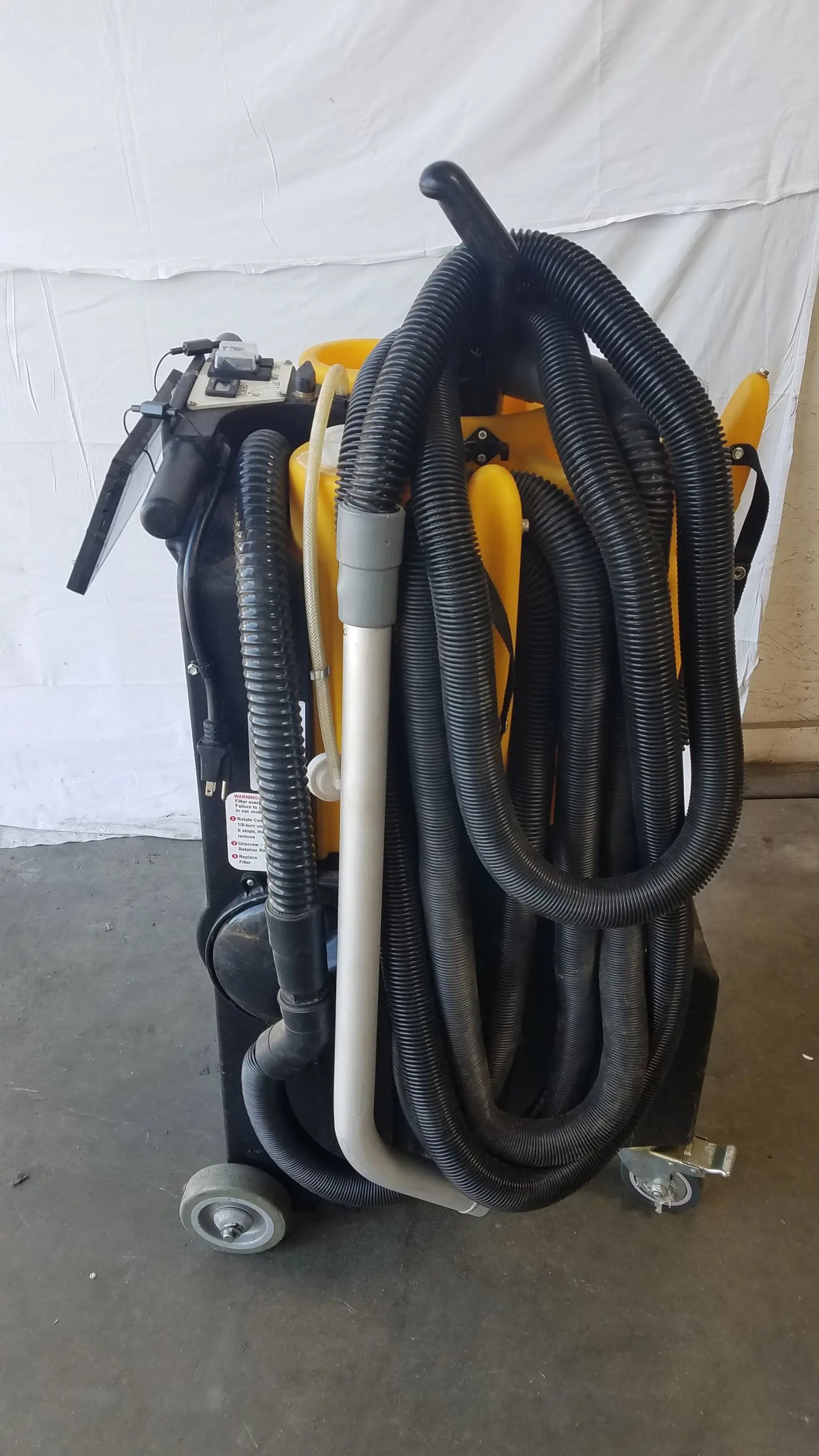 Black and yellow Kaivac wet dry vacuum cleaning system with multiple hoses coiled around its industrial body