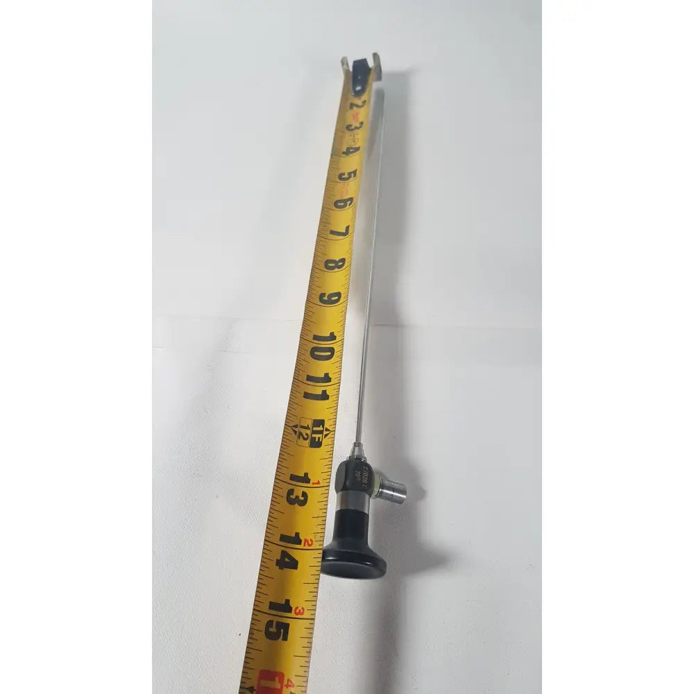 A slender metallic karl storz 27020 c hopkins 70 degree cystoscope with black ergonomic handle next to yellow measuring tape