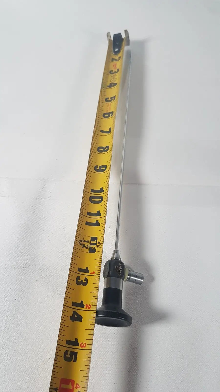 A slender metallic karl storz 27020 c hopkins 70 degree cystoscope with black ergonomic handle next to yellow measuring tape