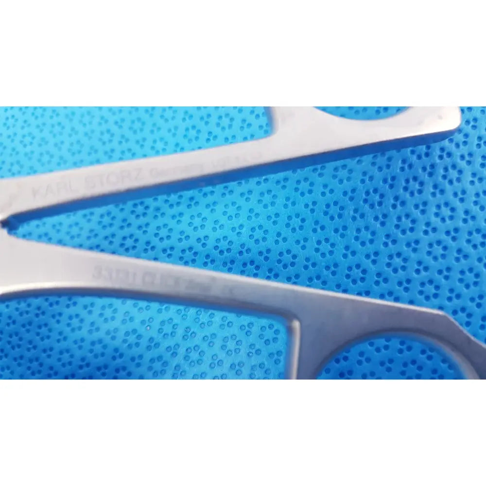 Silver karl storz laparoscopic surgical forceps with clickline handle resting on textured blue perforated surface