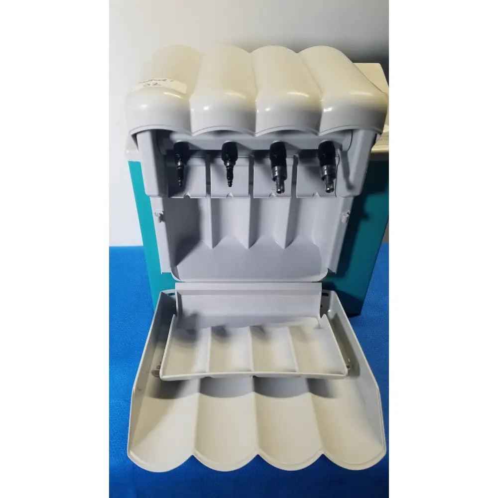 Cream-colored plastic kavo quattrocare 2104a dental handpiece maintenance unit with four black dispensing nozzles and tray