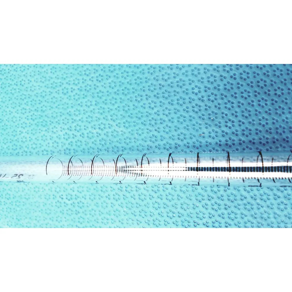 A kimax 25ml clear plastic syringe with black markings and white plunger on a textured blue surface for lab use