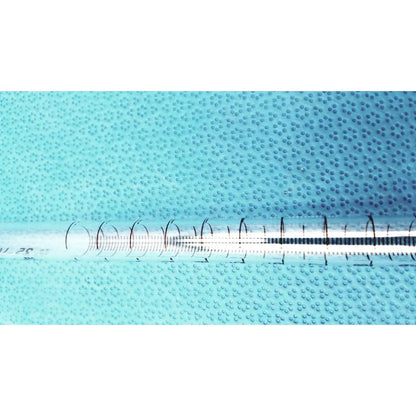 A kimax 25ml clear plastic syringe with black markings and white plunger on a textured blue surface for lab use